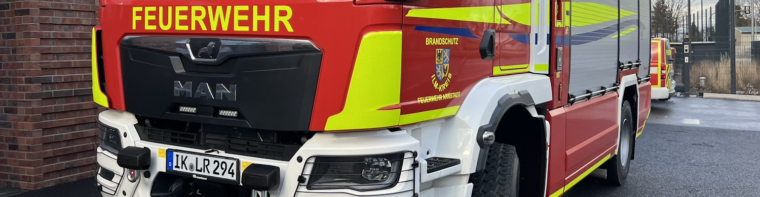 fahrzeug-arnstadt Rotes Feuerwehrfahrzeug der Marke MAN mit gelben und grünen Streifen, sichtbar ist das Feuerwehrwappen.