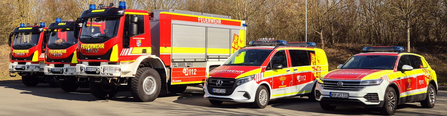ftz-immelborn Drei Feuerwehrfahrzeuge und zwei Einsatzfahrzeuge stehen auf einem Parkplatz. Die Fahrzeuge sind rot und gelb lackiert, mit Blaulicht auf dem Dach.